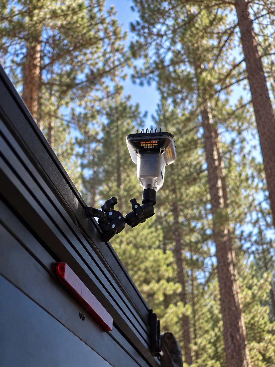 FireCrateUSA SuperClamp mounting a Devos LightRanger to a vehicle roof rack among tall pine trees